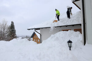 Godfrey Roofing, Snow and Ice Removal. Two Men Shoveling High Heavy Snow From A, House Roof.