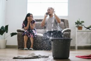 Roof Contractors in Ottawa. Water Drips Into Buckets In Living Room As Frustrated Couple sits in background.