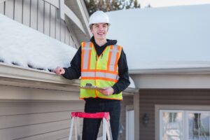 Roof Repairs. home inspector on a ladder while holding a clipboard during winter. Inspecting roof.