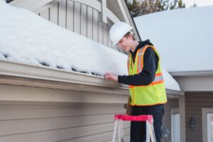 Fix Winter Damage With Godfrey Roofing: Ottawa Roofing Experts. Happy home inspector on a ladder while holding a clipboard during winter.