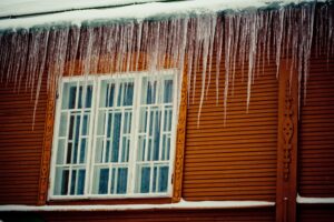 Winter Roof Repairs. Snow and Icicles and Ice Dam on Roof and Gutter.